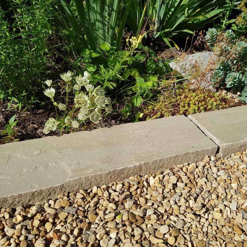 flat grey stone edging bordering a green foliage flower bed.